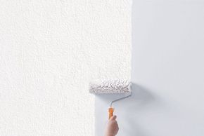 Hand trägt weiße Farbe mit Rolle auf